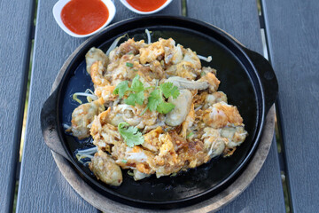 Thai style of Fried Oyster Omelete on black plate with spicy sauce.