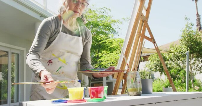 Asian senior woman wearing apron and painting in garden on sunny day