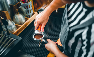 Fototapeta na wymiar Barista holding portafilter and coffee tamper making an espresso coffee in cafe
