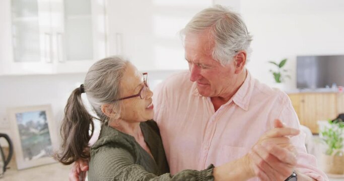 Happy diverse senior couple holding hands and dancing in kitchen