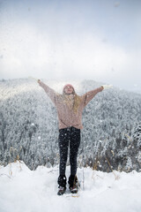 Happy young woman in warm clothes playing with the snow in the mountains. Winter holiday concept.