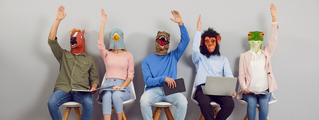 Team in funny animal masks demonstrate unanimous agreement as they vote for good suggestion at work. Group of people in horse, bird, dinosaur, monkey and frog heads sitting in row and raising hands up