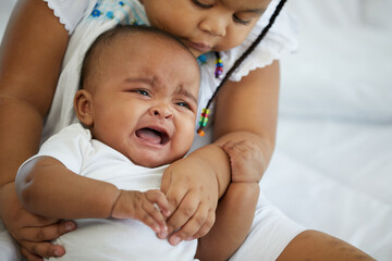 African newborn baby crying and her sister soothing to stop crying on bed