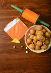 Makar Sankranti greeting card cover. Bowl of Tilgul, a kite and Chakri placed on wooden background, shot from above.