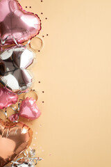 Fototapeta premium Valentine's Day decor concept. Top view vertical photo of stylish heart shaped balloons silver serpentine and shiny confetti on isolated pastel beige background with copyspace