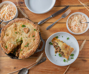 Steak and cheese pie baked in a cast iron pan. Served with fresh coleslaw on wooden table. Flat lay