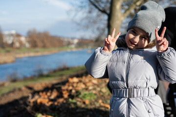 Baby girl showing two fingers at warm autumn weather, outdoor activity.