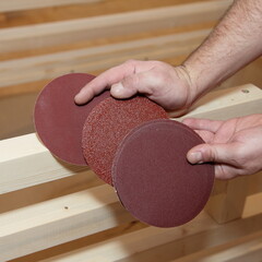 Three sandpaper circles with different grain sizes in carpenter hands. Wooden furniture grinding...