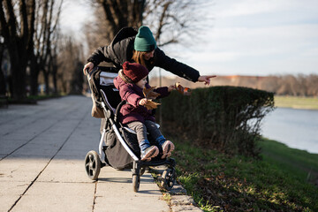 Young woman in city park with baby stroller. Warm autumn weather for outdoor activity.
