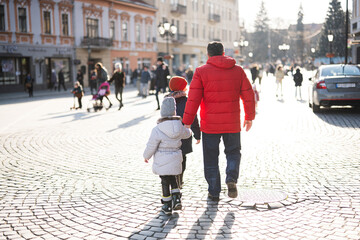 Back of grandfather with grandson and granddaughter walking  in city square.
