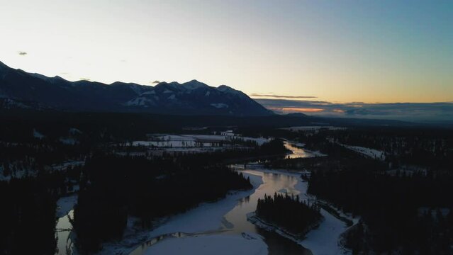 Aerial Unveiling of Gorgeous Winter Landscape During Golden Hour: Bird's Eye View of Reflective River and Stately Mountains in British Columbia, Canada
