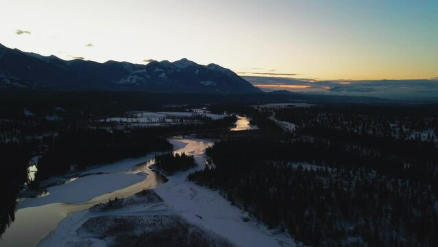 Exquisite Winter Landscape During Golden Hour: Aerial Panning Left of Shimmering River and Elegant Mountains in British Columbia, Canada