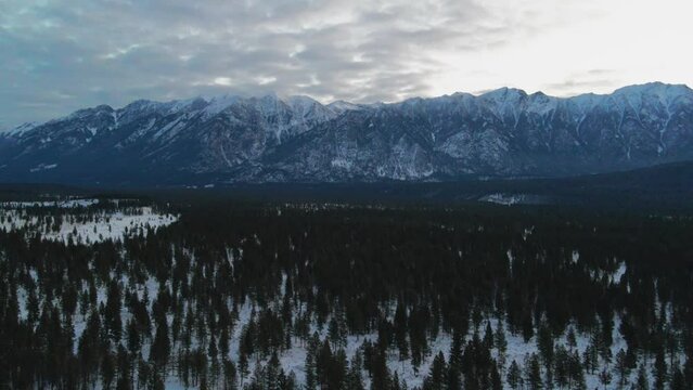 Aerial Side Drift Shot of Impressive Snow Covered Mountains and Forests on a Cloudy Day During Sunrise in British Columbia, Canada: Stunning Winter Landscape