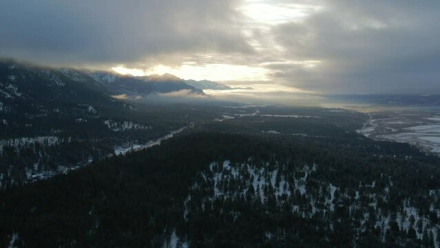 Aerial View of Cariboo Highway 95 Running into the Horizon Surrounded by Impressive Snow Covered Mountains and Forests During Warm Sunrise: Panoramic Scene of Spectacular Winter Landscape