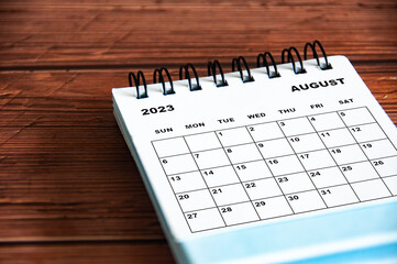 August 2023 white desk calendar on wooden table background. Calendar concept and copy space