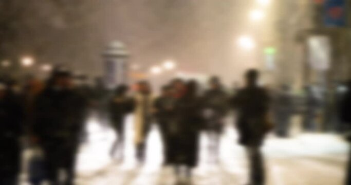 Defocused blur scene of people walking on the covered by snowalls street during a cold winter at night in the city