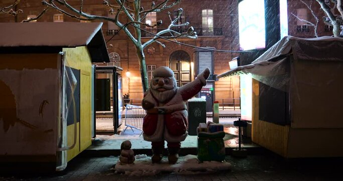 Lonely Santa Claus statue at night between close market stalls at annual Christmas market in Strasbourg - pedestrians in background