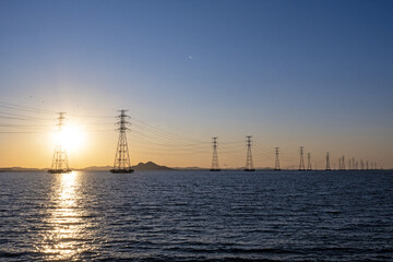 바다 위에 설치된 송전탑과 그 뒤에 떠있는 태양