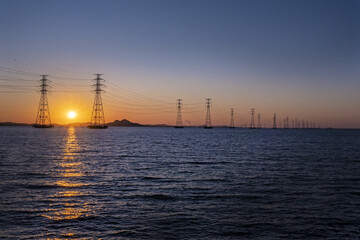 바다 위에 설치된 송전탑과 그 뒤로 지는 태양