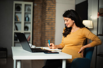 Beautiful pregnant woman working on laptop. Young businesswoman working in her office..