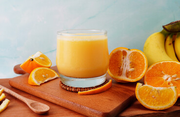 Orange fruit smoothie in a glass with fresh orange slices on wood