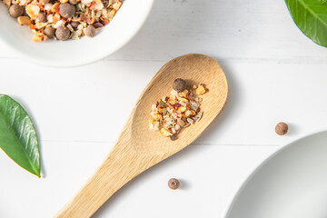 various spices on a wooden spoon on white wooden background with other white kitchenware and green leaves. High quality photo