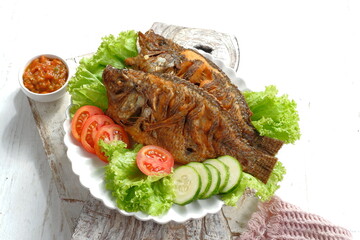 Fried Tilapia or Ikan Nila Goreng. Served on white plate with lettuce,cucumber and tomato on white...