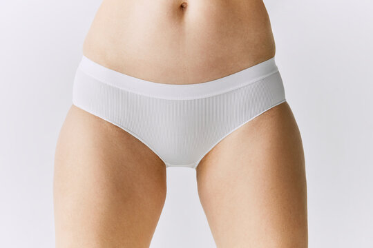Cropped image of female body, belly, buttocks in underwear posing over grey studio background. Front view