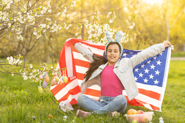 Girl kid in rabbit bunny ears on head with colored eggs and american flag. easter