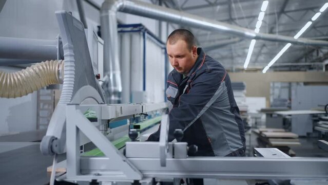 adult man working in workshop of modern furniture factory, controlling automatic cutting machine