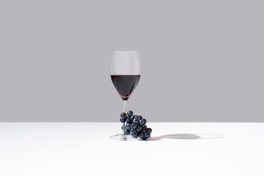 Copa de vino tinto y racimo de uvas negras sobre fondo gris