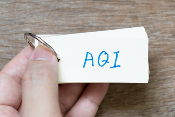 Hand hold flash card with handwriting in word AQI (Abbreviation of air quality index) on wood...