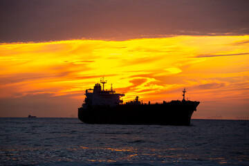 transport ship in front of sunset with clouds and wind turbines at the horizon