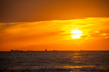 sunset with clouds above sea with transport ships and wind turbines at the horizon