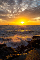 colorful sunset above the sea with cloudy sky and breakwater with spray in the foreground