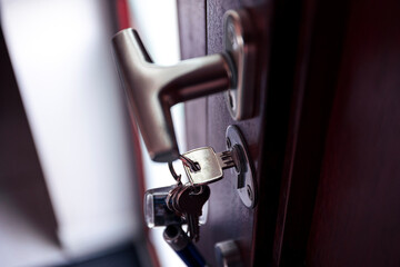A portrait of a key in a key hole turned horizontally to lock or unlock a wooden front door with a T shaped door handle to keep other people, thieves or burglars out for safety and security.
