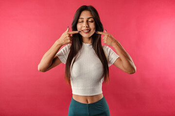 Portrait of cute dark-haired woman wearing casual top isolated over red background smiling and showing finger pointing white teeth. Dental health concept.