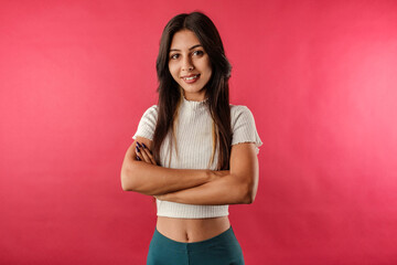 Obraz premium Happy brunette woman wearing casual top isolated over red background poses with arms crossed, looking at the camera. Looks confident and accomplished.