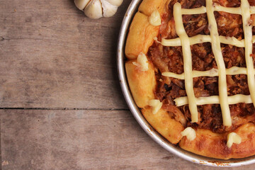 Pizza topped with melted cheese and ham served on a wooden table with a cropped image. 
