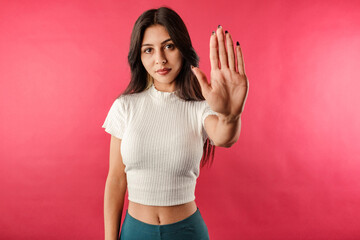 Young dark-haired woman wearing ribbed crop isolated over red background doing stop sing with palm...