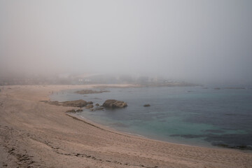 A blue transparent ocean with a rocky bottom in the fog. Sandy beach without people.
