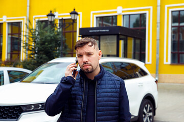 Mid adult european white male man with goatee beard talks on smartphone on street. Frowning tense sullen or sad concentrated man. Waist up lifestyle business portrait, difficult conversation - obrazy, fototapety, plakaty