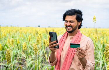 happy smiling Young farmer at field with making online payment using credit card on mobile phone - concept of e-commerce, online banking service and technology