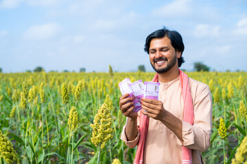Happy farmer couting money or currency at agricultural farmland - concept of profit or earnings,...