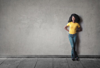 Obraz na płótnie Canvas young black woman leaning against a gray wall