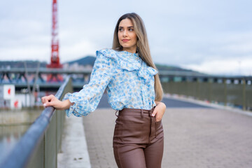Obraz premium Portrait young woman on a city river bridge, lifestyle concept, blue shirt and brown pants