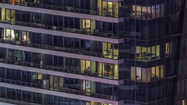 Windows lights in modern office and residential buildings timelapse at night. Multi-level skyscrapers with illuminated rooms inside. Some people on a balconies