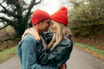 A couple of a man and a woman in red hats gently hug.