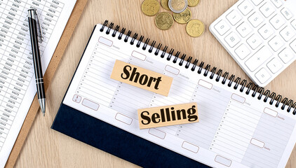 SHORT SELLING word written on wooden block on planner with coins, clipboard and a calculator