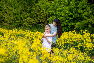 Fototapeta premium A young mother hugs her son in a field with yellow flowers